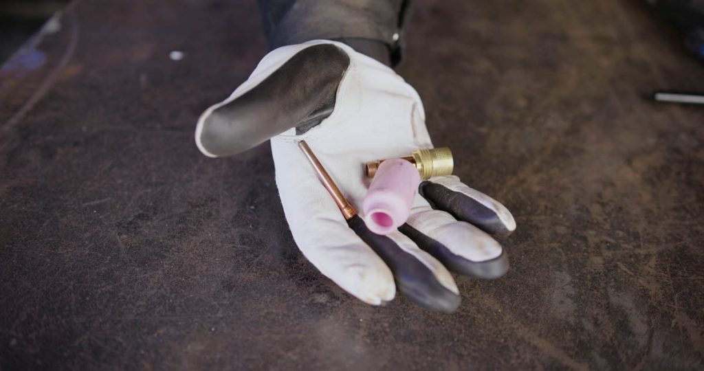 Hand holding TIG consumables: collet, gas lens and ceramic cup
